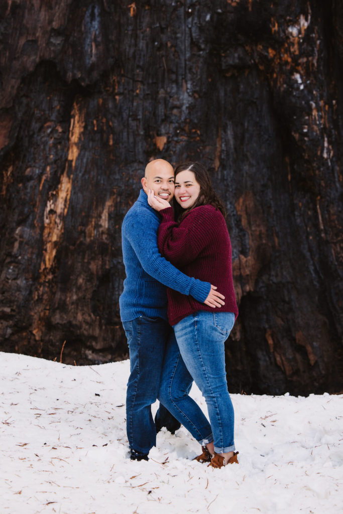 couple standing in front of a tree in the snow