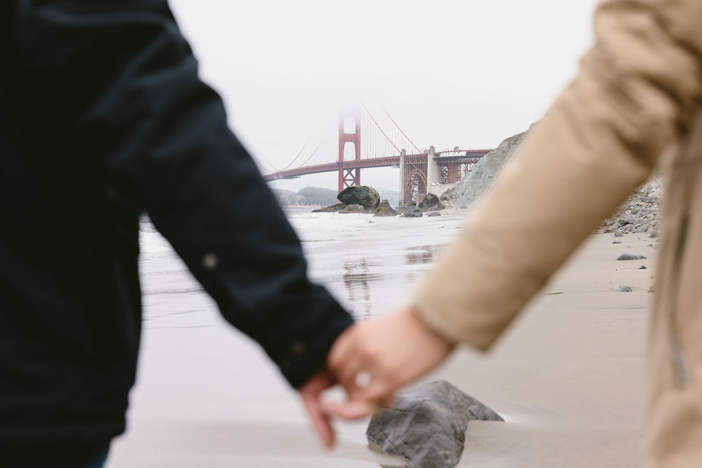 Couple holding hands on Baker Beach in San Francisco California after planning for engagement