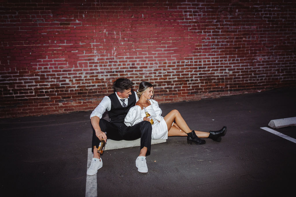 Bride and groom drinking coronas in front of brick wall in Fresno, CA