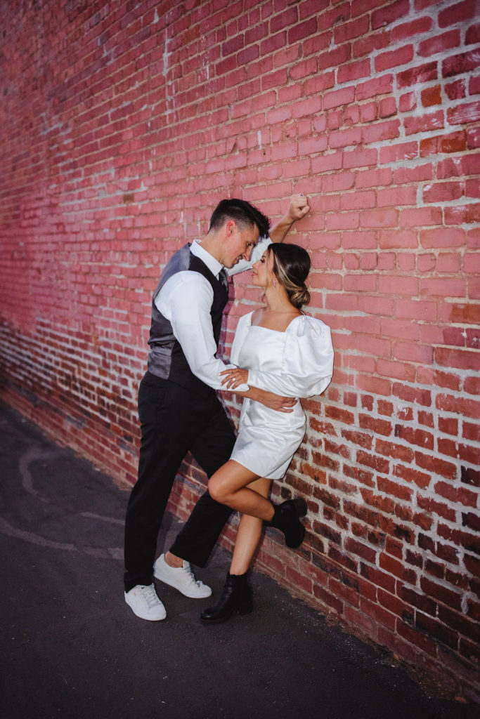 Bride and groom leaning against brick wall