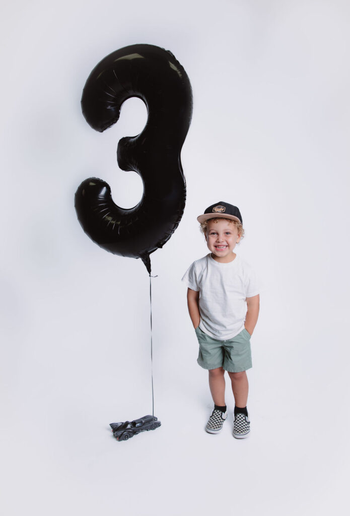 Little boy posing with 3 year balloon for studio birthday portraits