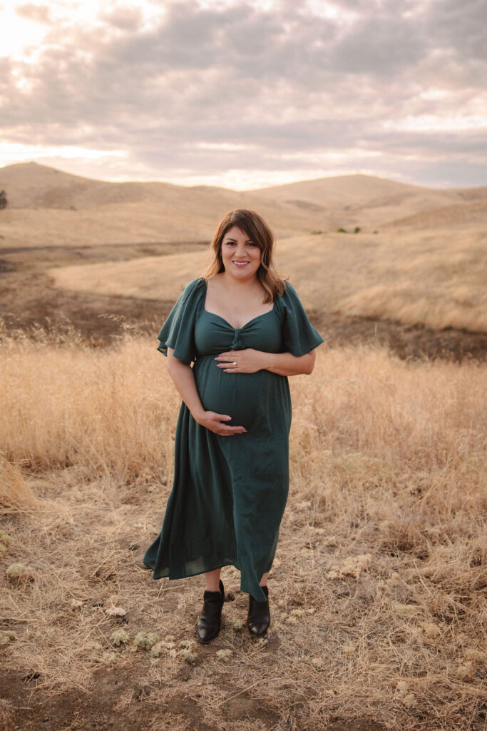 Mother holding her pregnant belly during sunset in a field