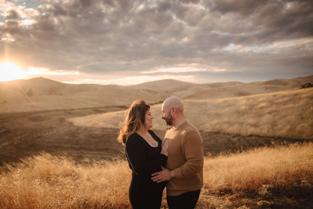 Man and pregnant woman posing for photos in a field at sunset
