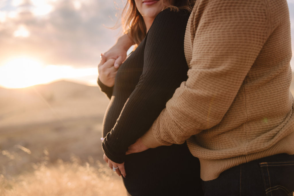 Man and pregnant woman posing for photos in a field at sunset