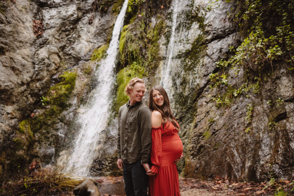 couple in front of waterfall during dreamy maternity photos