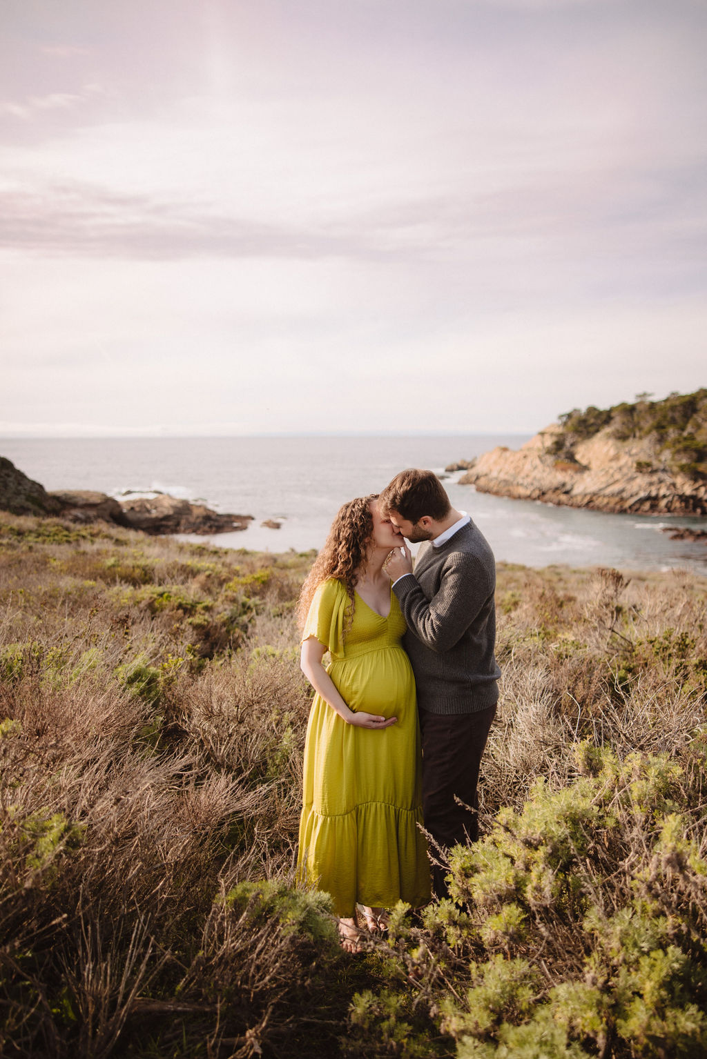 A couple embracing on a coastal landscape with the sea in the background at Big Sur
