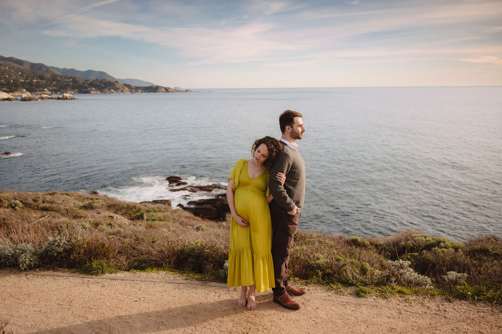 A couple embracing on a coastal landscape with the sea in the background at Big Sur