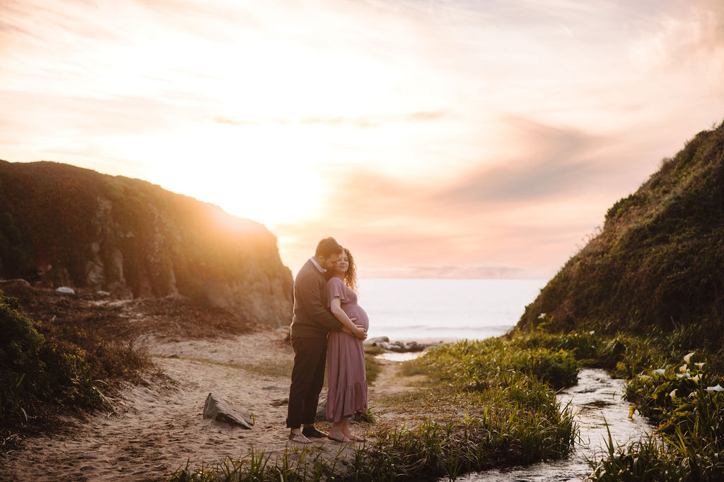 A couple at the beach at sunset, with flowers and a pathway in the foreground at Big Sur