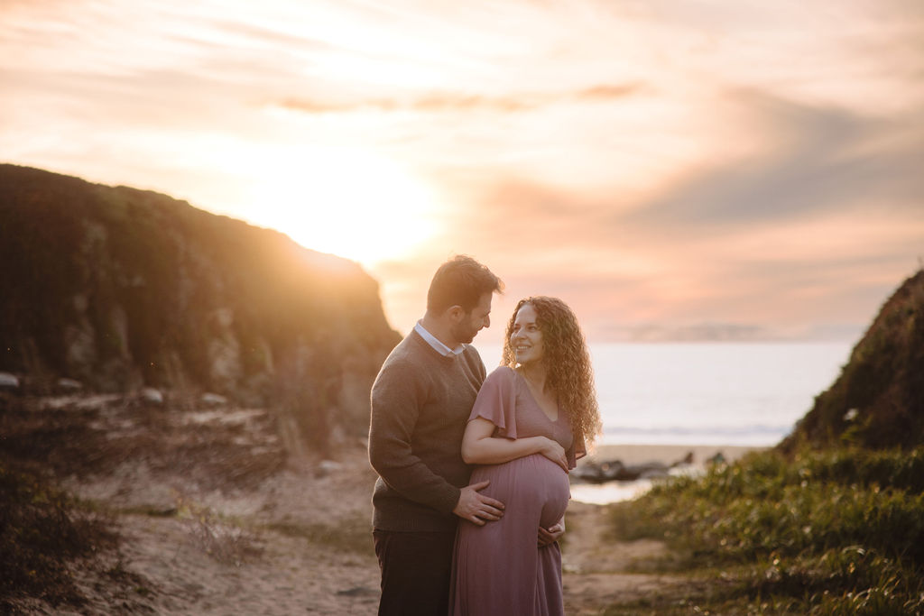 A couple expecting a child embracing each other at sunset on the beach at Big Sur