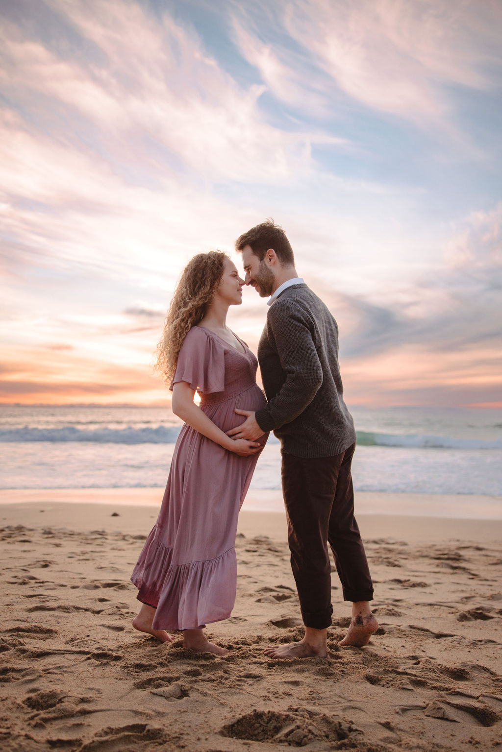 A couple holding hands and walking on a beach at sunset during their beach maternity photos