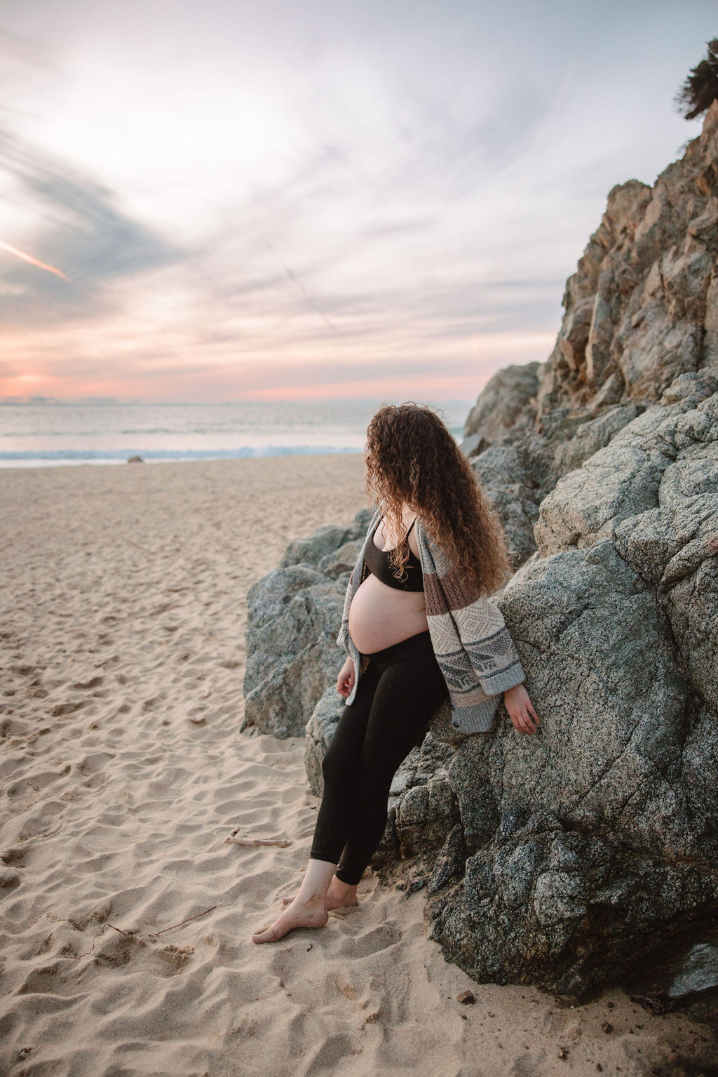 Pregnant woman standing on the beach at sunset, cradling her belly.