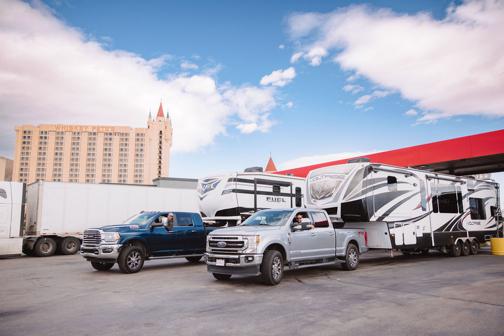 Trucks refueling at a station with large rvs parked beside them, under a blue sky with whiskey pete's hotel in the background.