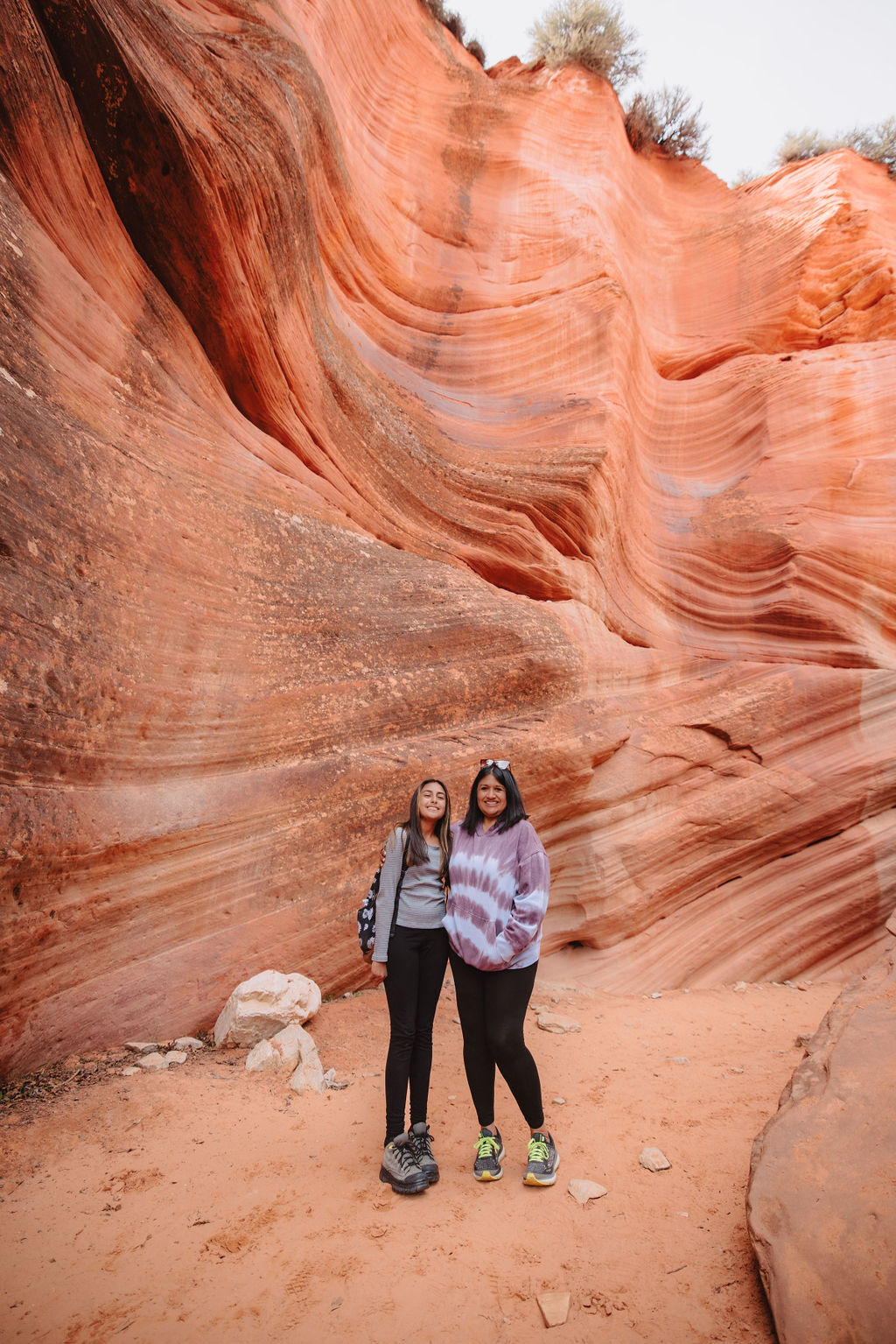 Two women standing together in front of a striated red rock formation in a canyon at zion national park