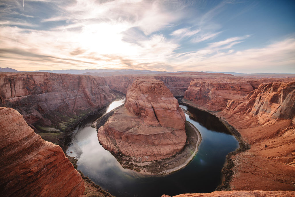 View of horseshoe bend with the colorado river winding through a deep canyon under a vast, cloudy sky at sunset.