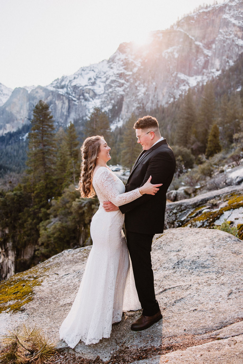A couple embracing and smiling at each other at their elopement in a mountainous backdrop bathed in golden sunlight for their yosemite national park elopement 