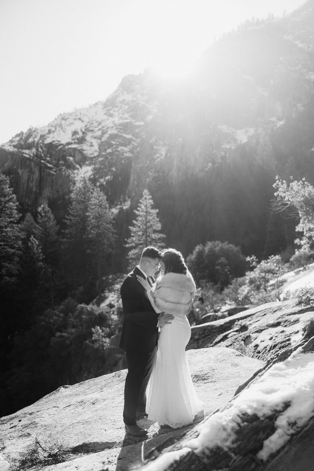 A couple in wedding attire dancing on a mountain overlook with scenic cliffs in the background.