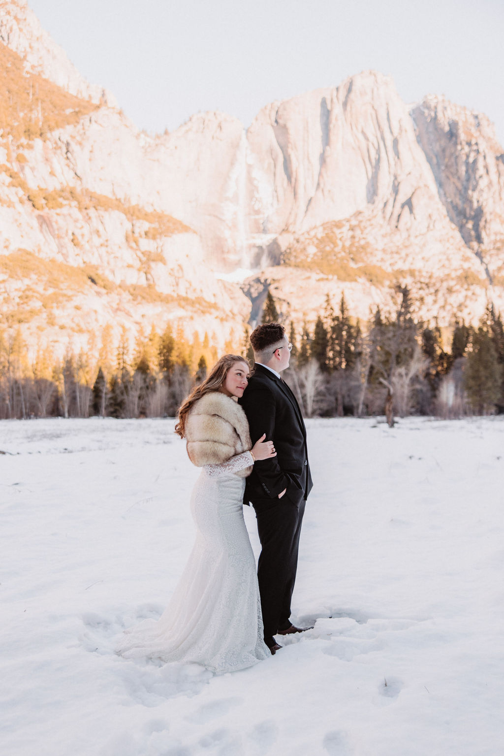 A couple holding hands and walking in the snow with a mountainous backdrop at Yosemite National Park