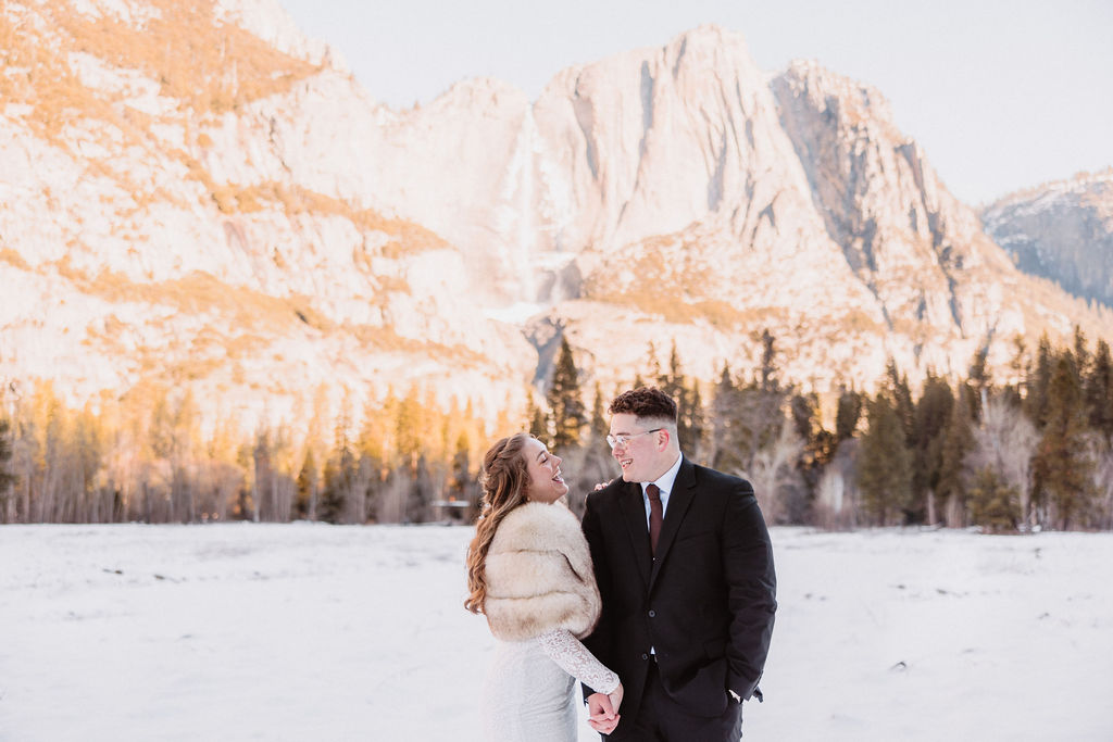 A couple holding hands and walking in the snow with a mountainous backdrop at Yosemite National Park