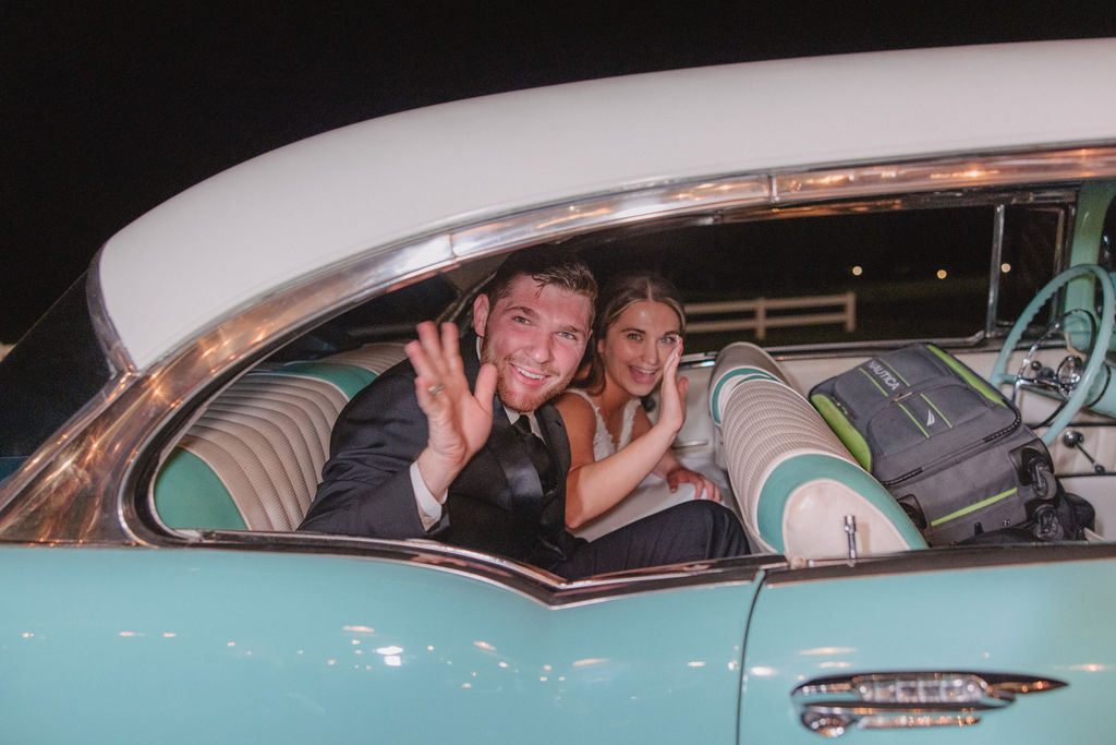 A man drives a vintage mint green car with a young couple smiling in the back seat at night after their wedding at deep in the heart farms