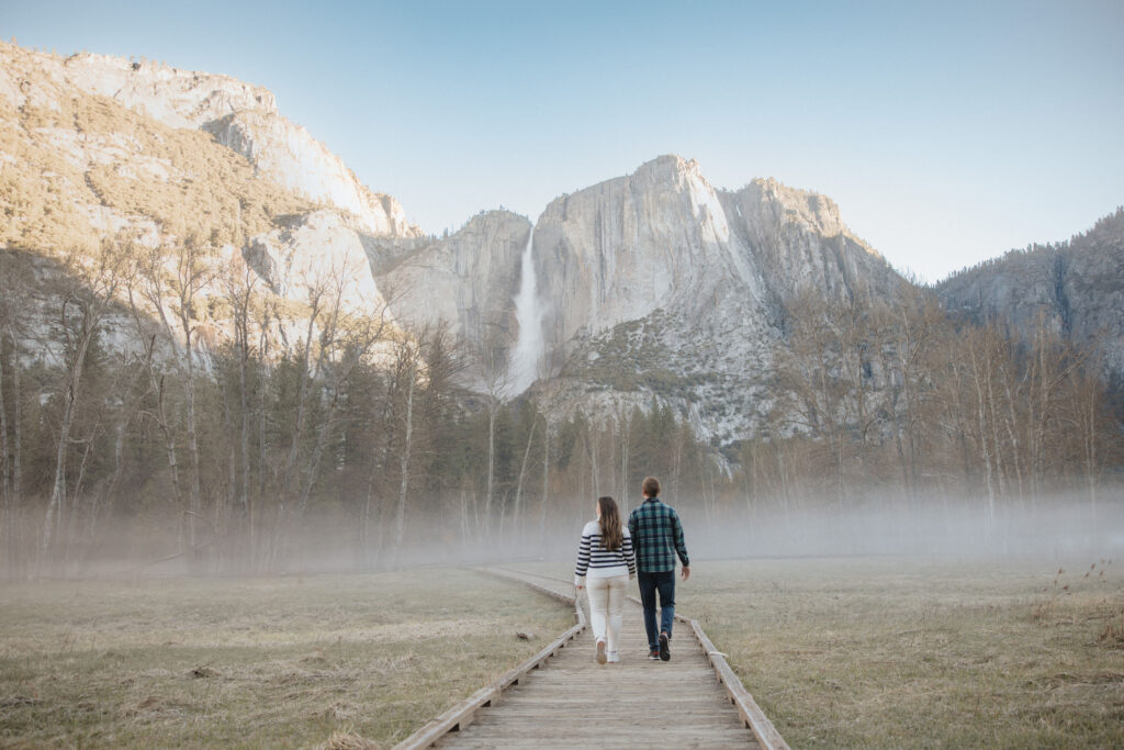 Couple walking on boardwalk during their engagement photoshoot with fog in yosemite. 