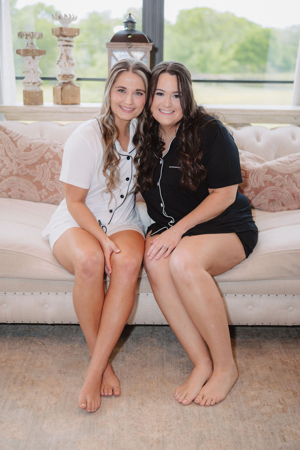 bridesmaid matching black outfits and one person in white sit on a couch, smiling and engaging in conversation at a wedding