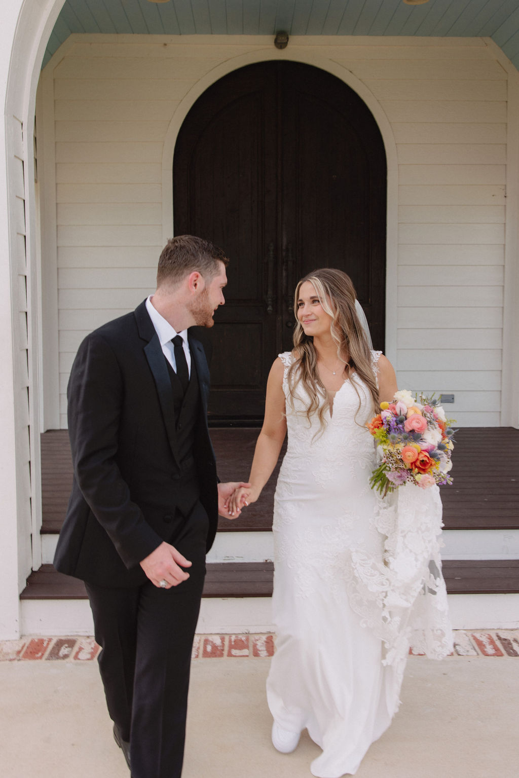 Bride and groom holding hands, walking, and looking at each other in front of deep in the heart farms wedding venue 
