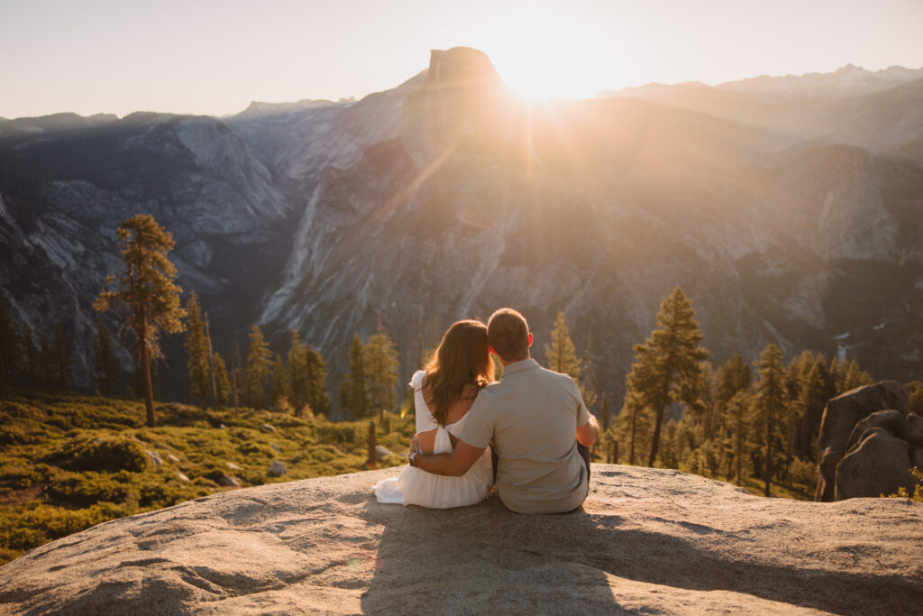 Couple sitting on rock looking at the sunrise at glacier point in yosemite. 