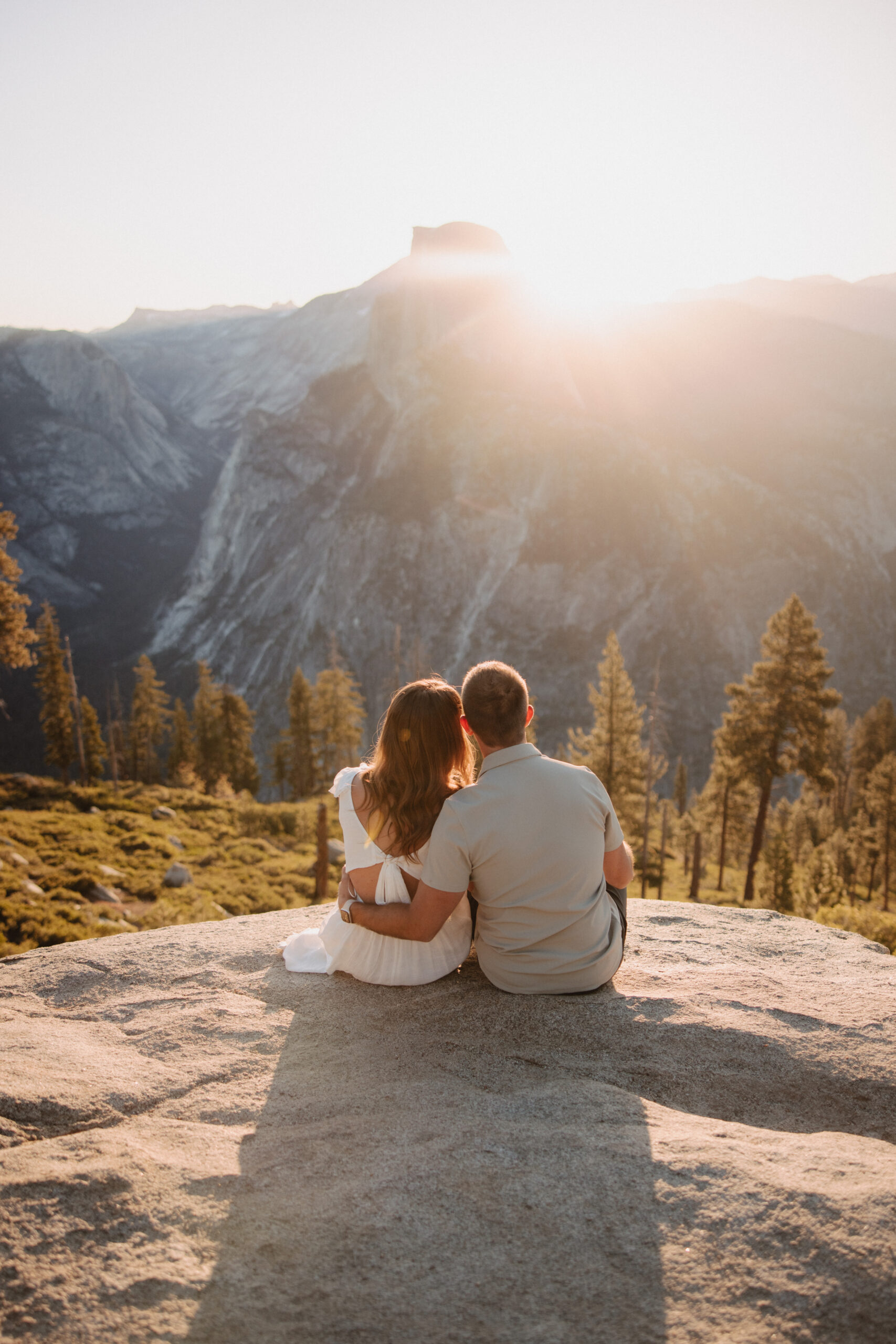 Couple watches sunrise peek over half dome during their engagement session at glacier point in yosemite national park