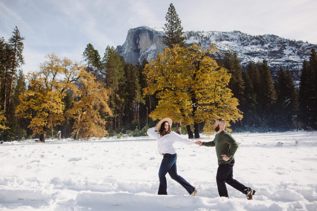 Couple running in the snow during their engagement photoshoot in yosemite with half dome in the background. 