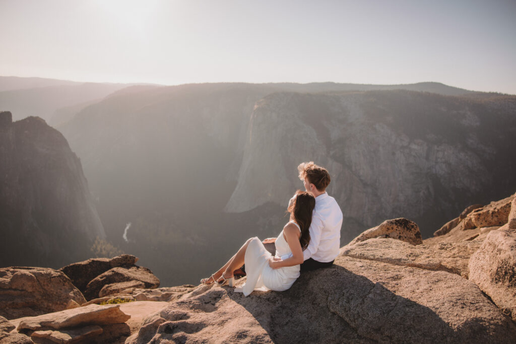 Taft point engagement photoshoot with El Cap in the background. Couple sitting on rock looking out in the distance. 