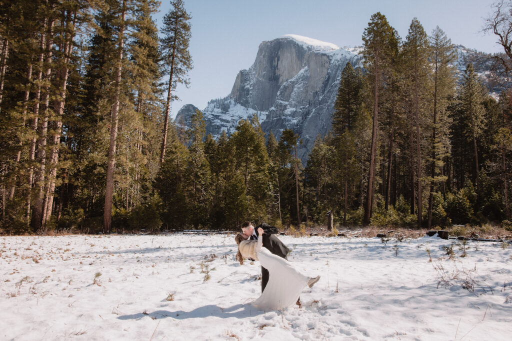 Bride and groom doing a dip pose in front of half dome in yosemite valley after their elopement ceremony. 