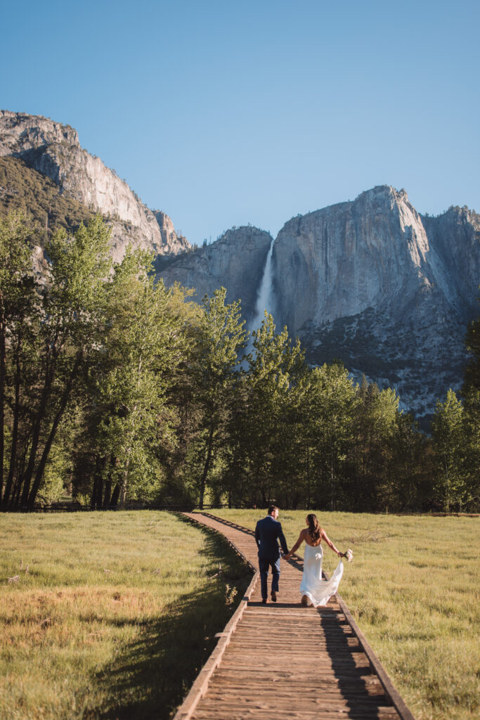 Bride and groom running in the spring after their elopement ceremony in yosemite at cooks meadow with yosemite falls in the background.