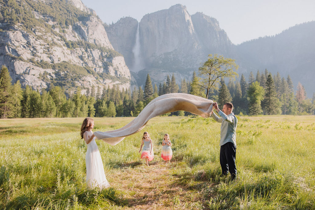 Family at Yosemite National park for their documentary style family photos walking into meadow and setting up a picnic 