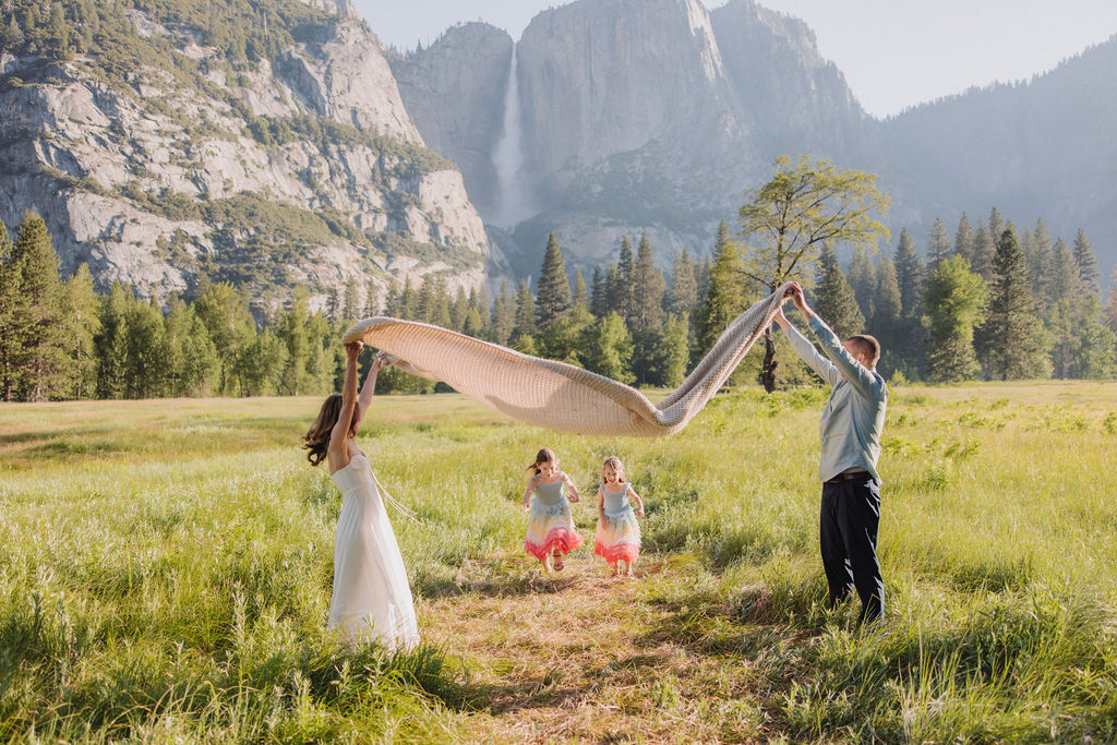 Family at Yosemite National park for their documentary style family photos walking into meadow and setting up a picnic 