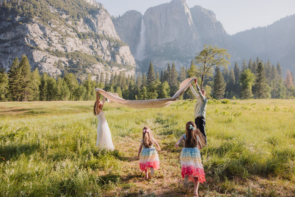 Family at Yosemite National park for their documentary style family photos walking into meadow and setting up a picnic 