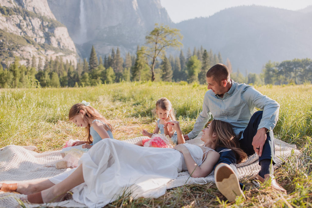 Family at Yosemite National park for their documentary style family photos walking into meadow and setting up a picnic 