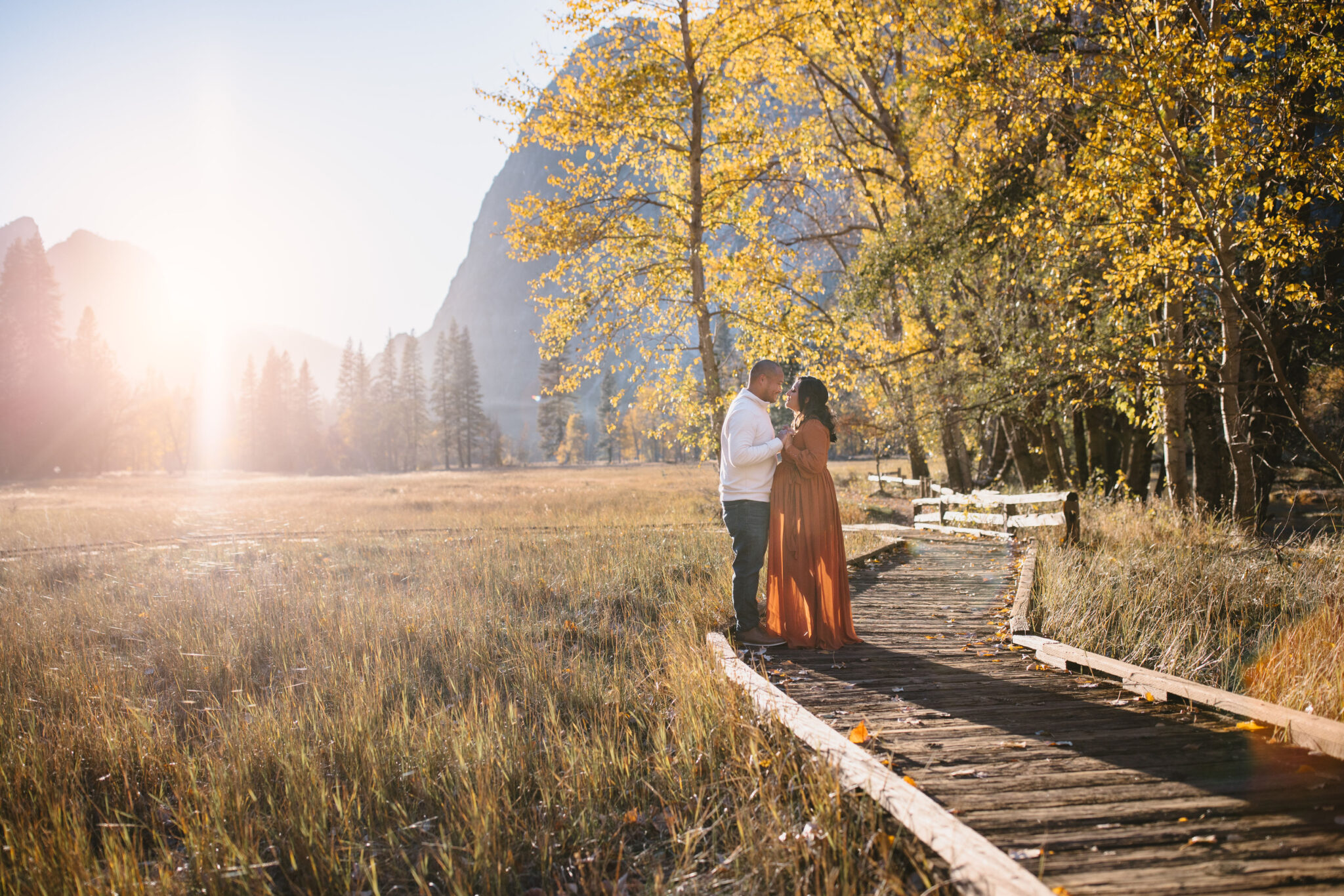 A couple stands on a wooden path surrounded by autumn foliage, with mountains and sunlight in the background | Ultimate Yosemite Visitor Guide 