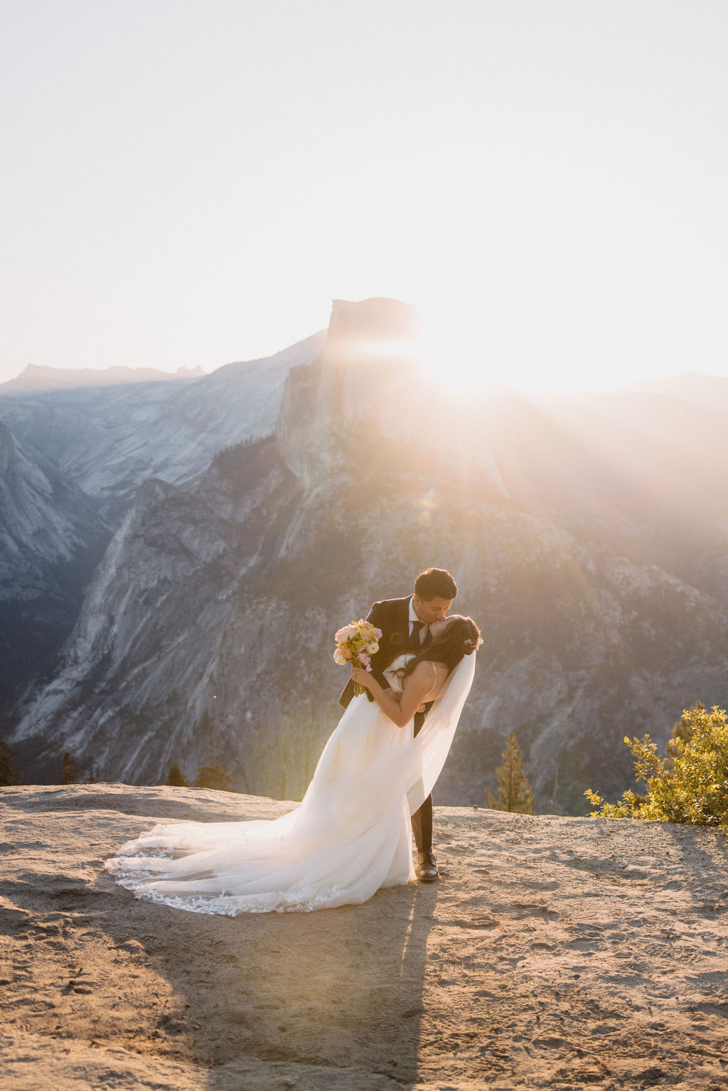 A bride and groom share a kiss at sunset on a rocky outcrop with mountains in the background for a Yosemite elopement