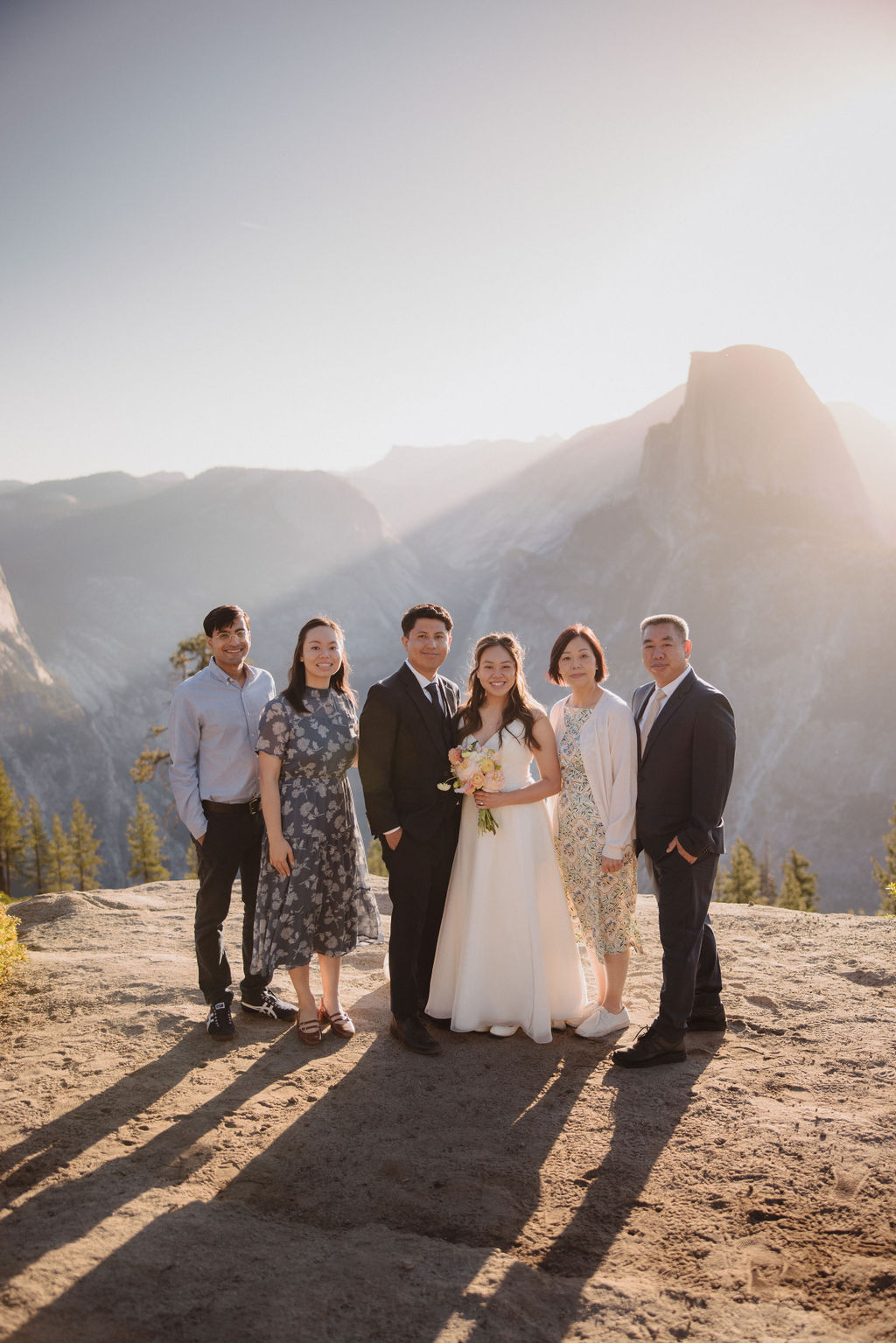 A group of six people, including a bride and groom, pose together outdoors with mountains in the background in Yosemite for an elopement