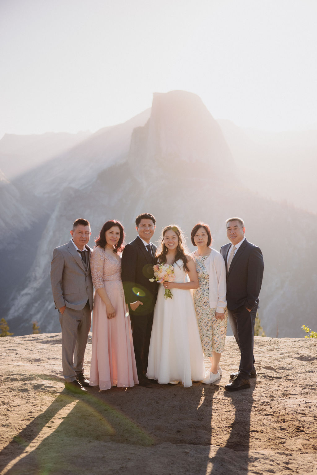 A group of six people, including a bride and groom, pose together outdoors with mountains in the background in Yosemite for an elopement