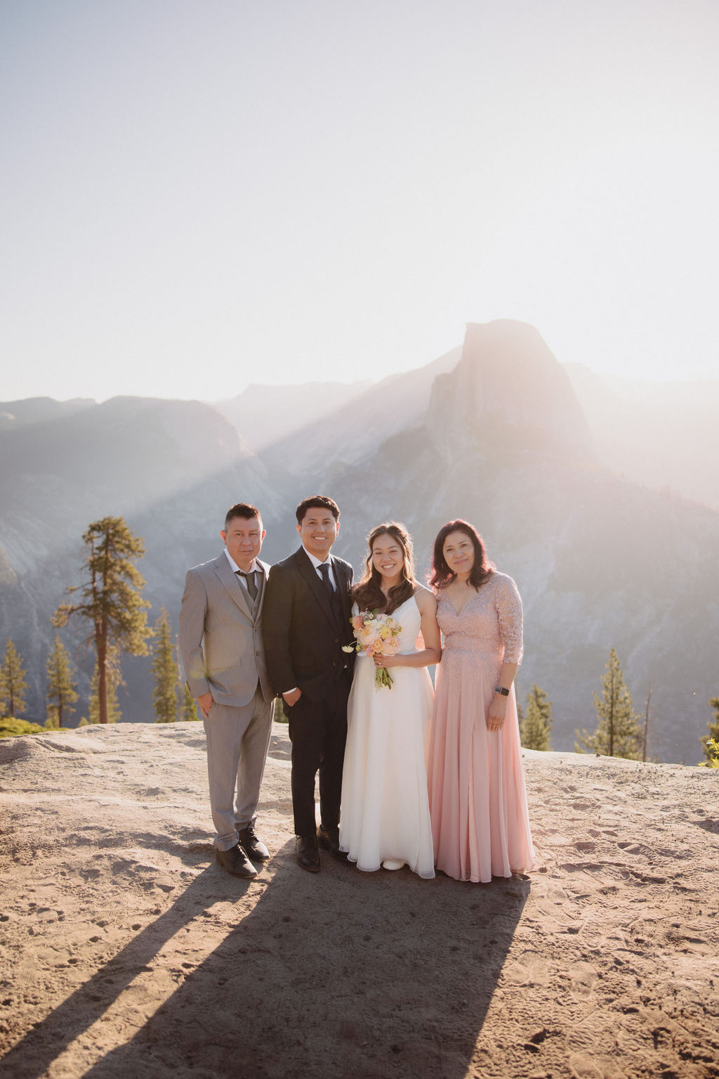 A group of six people, including a bride and groom, pose together outdoors with mountains in the background in Yosemite for an elopement