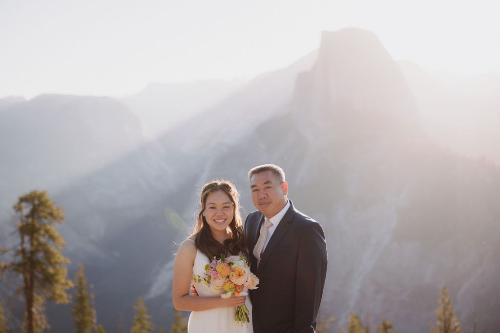 A group of six people, including a bride and groom, pose together outdoors with mountains in the background in Yosemite for an elopement