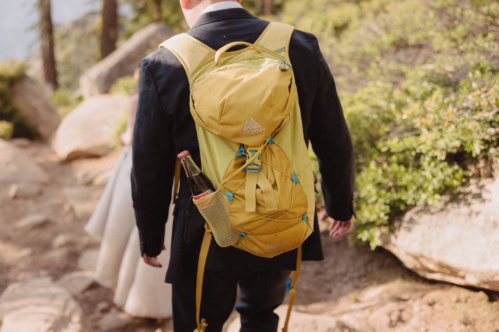 A couple in formal attire shares an intimate moment while standing on a log in a dense forest clearing with sunlight filtering through the trees in Yosemite