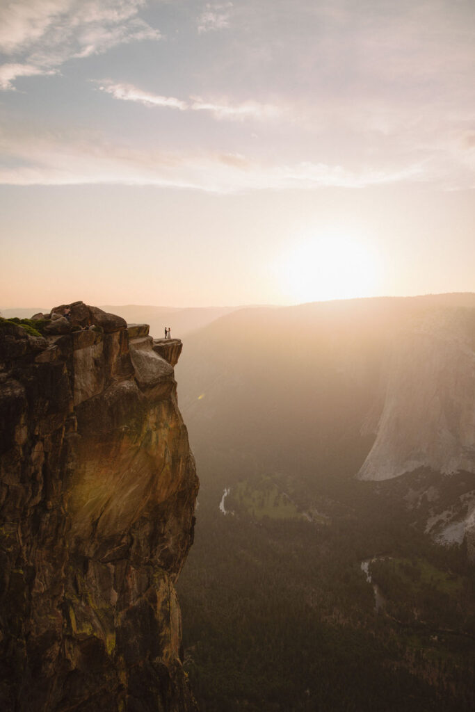 A couple in wedding attire shares a kiss at sunset on a cliffside for their yosemite elopement