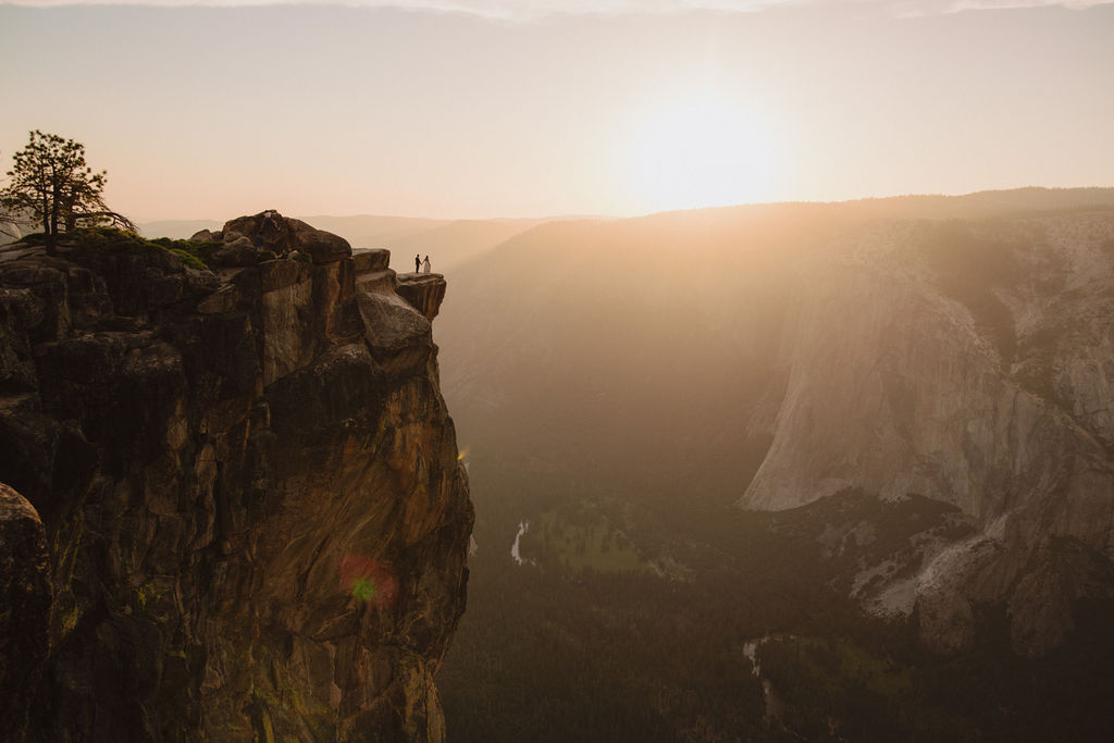 A couple in wedding attire embraces and kisses at sunset on a cliff with a mountain range in the background| tips for yosemite elopement