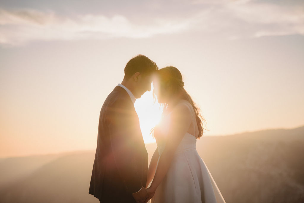 A couple in wedding attire shares a kiss at sunset on a cliffside for their yosemite elopement 