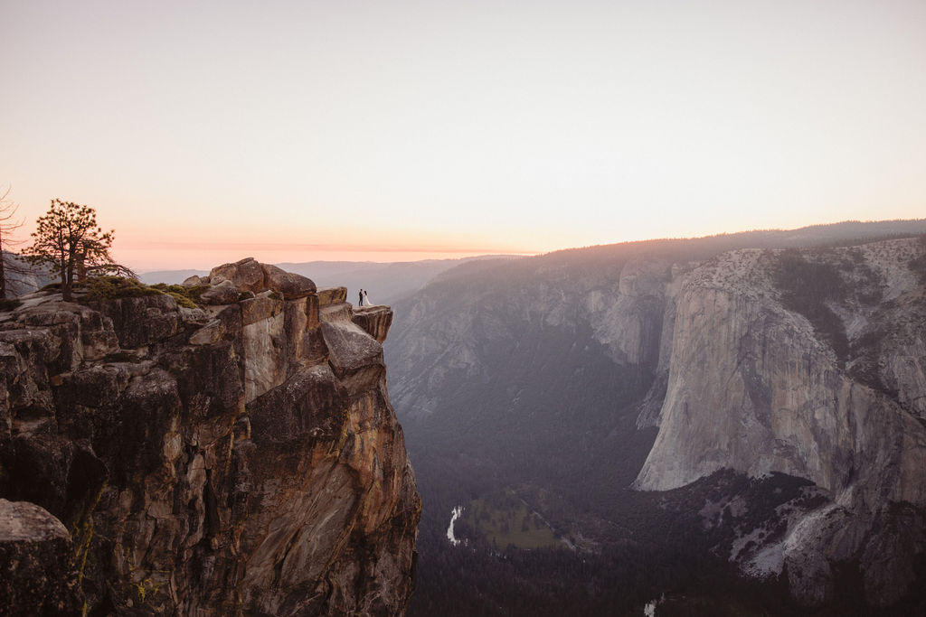 A person stands on the edge of a rocky cliff at sunrise, with a vast canyon and distant mountains in the background. | Tips for planing a stress free yosemite elopement