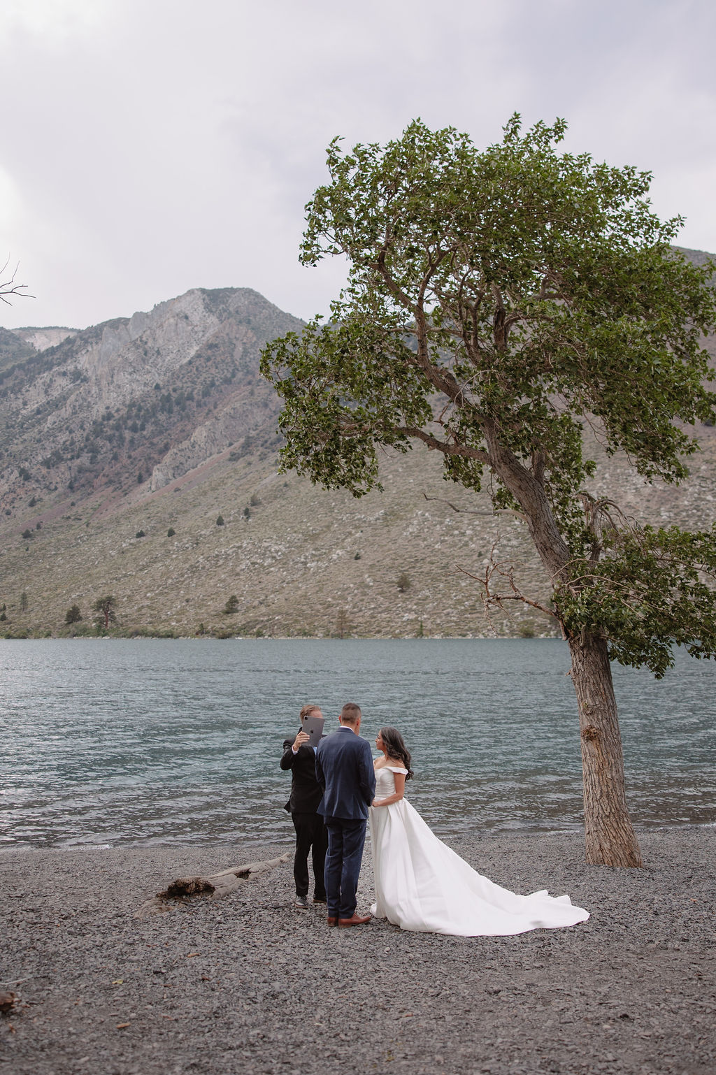 A wedding ceremony by a lakeside, with a couple in formal attire and a man officiating for a mammoth lakes elopement 