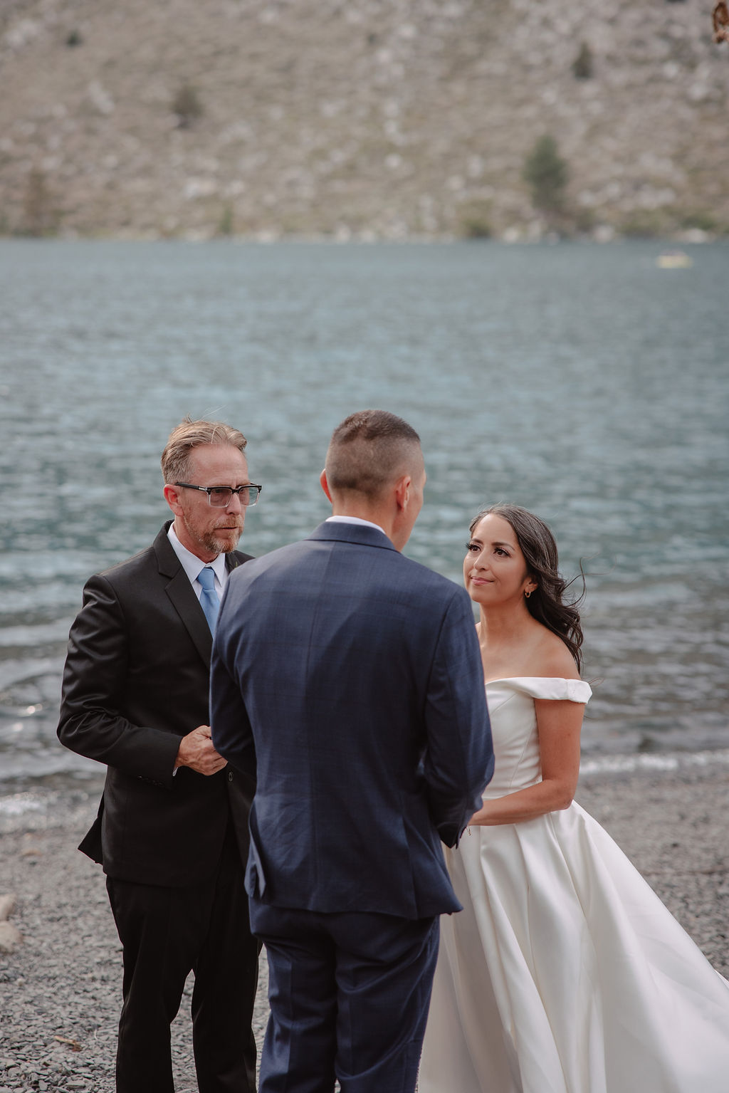 A wedding ceremony by a lakeside, with a couple in formal attire and a man officiating for a mammoth lakes elopement 