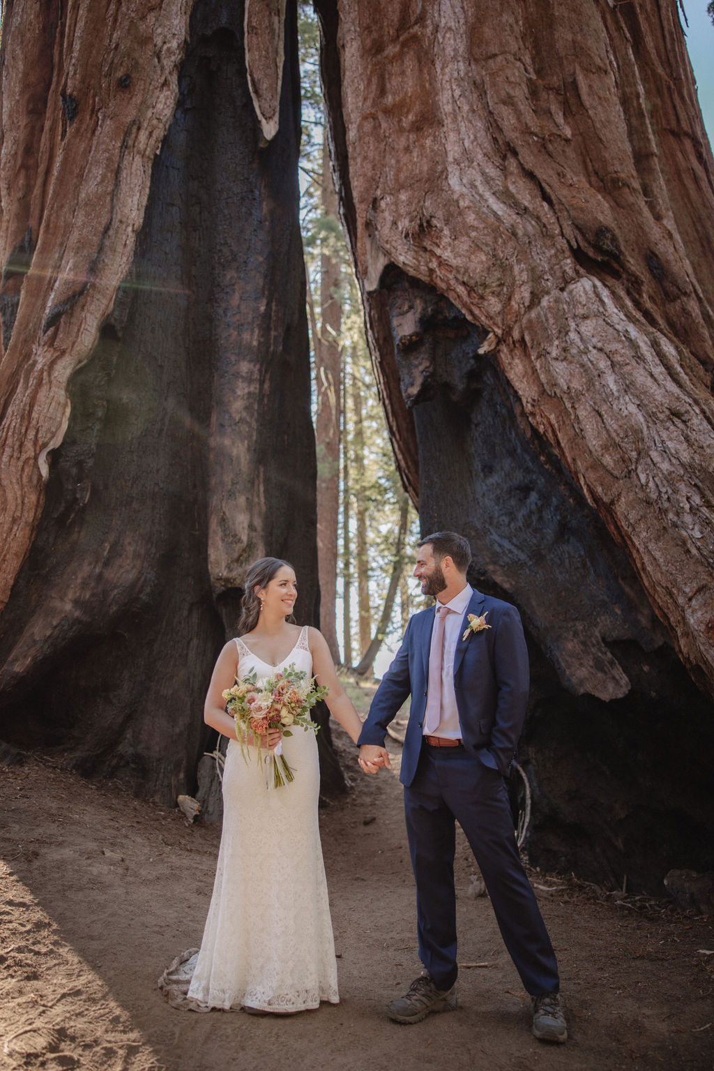 Two people in formal attire walk holding hands, each carrying backpacks with wooden signs. One sign reads "Just," and the other reads "Eloped.
Top 5 reasons to elope in sequoia national park